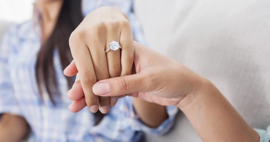 A woman elegantly displays a diamond ring on her hand, showcasing the beauty of rings in a refined manner.