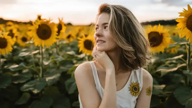 A woman stands amidst a vibrant sunflower field, embodying inspiration for creative ideas for sunflower tattoos.